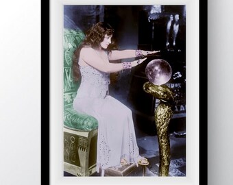 May include: A framed vintage photograph of a woman in a long white dress, seated on a green chair, with her hands outstretched towards a crystal ball. The crystal ball rests on a golden serpent-shaped stand. The image has a vintage, mystical theme.