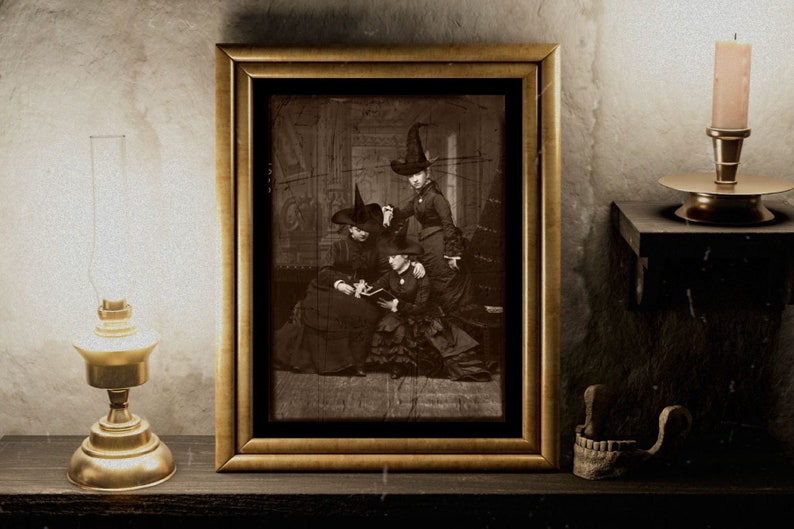 May include: A framed sepia-toned photograph of three women wearing witch hats. The women are sitting in a room with a dark wood floor and a patterned wallpaper. The photo is slightly faded and has a vintage look.