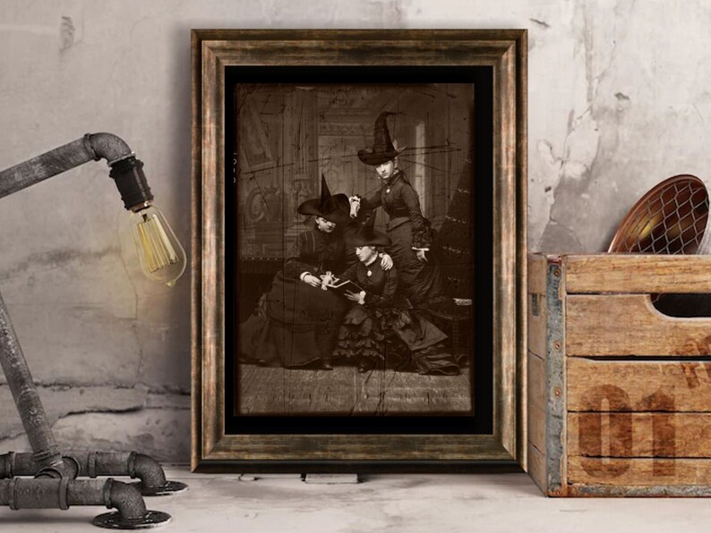 May include: A vintage black and white photograph of three women dressed as witches. The women are wearing long dresses and pointed hats. The photo is framed in a brown wooden frame.