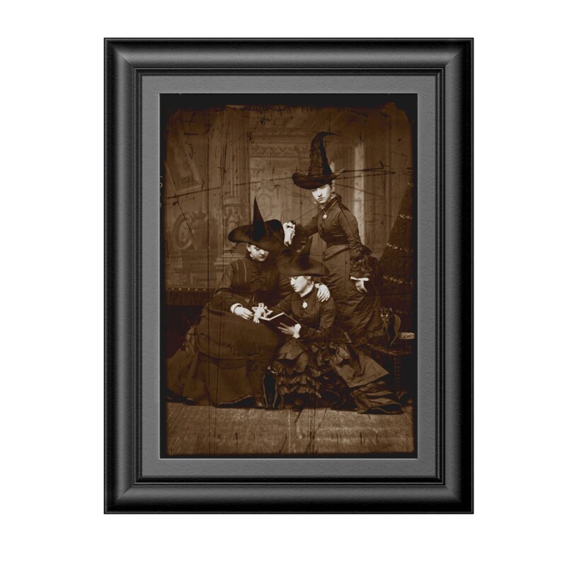 May include: Three women wearing black witch hats and long dresses are sitting together in a vintage sepia-toned photograph. The women are looking at a book in their laps. The background is a faded, textured wall.