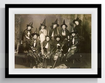 May include: A vintage black and white photograph of a group of women dressed as witches for Halloween. They are wearing black pointed hats, long black robes, and holding broomsticks. The photo is taken in a dimly lit room with a gothic backdrop.