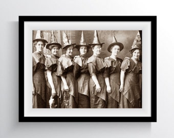 May include: A vintage black and white photograph of eight women dressed in witch costumes for Halloween. They are wearing pointed hats and long dresses. The photo is framed in a black frame.