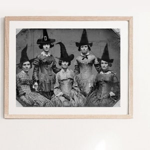 K&ouml;nnte beinhalten: Ein Schwarzwei&szlig;-Foto aus der Zeit von f&uuml;nf Frauen in Hexenh&uuml;ten und Kleidern. Die Frauen stehen in einer Gruppe und schauen in die Kamera.