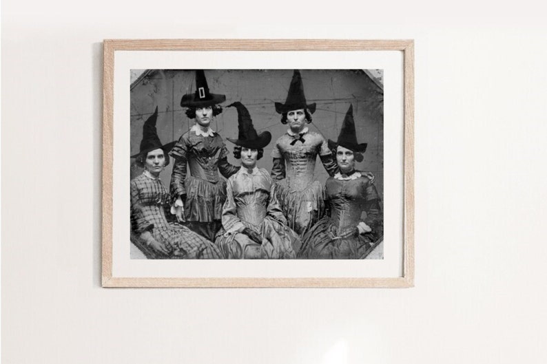 K&ouml;nnte beinhalten: Ein Schwarzwei&szlig;-Foto aus der Zeit von f&uuml;nf Frauen in Hexenh&uuml;ten und Kleidern. Die Frauen stehen in einer Gruppe und schauen in die Kamera.