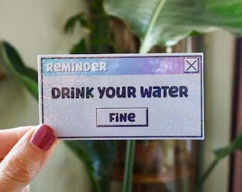 May include: A holographic sticker with a blue, pink, and white gradient. The sticker is shaped like a computer pop-up window with the text "Reminder: Drink your water" and a button that says "Fine".