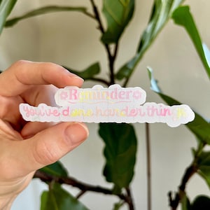 Könnte beinhalten: Ein weißer Aufkleber mit dem Text "Reminder: You've done harder things" in rosa und gelber Schrift.