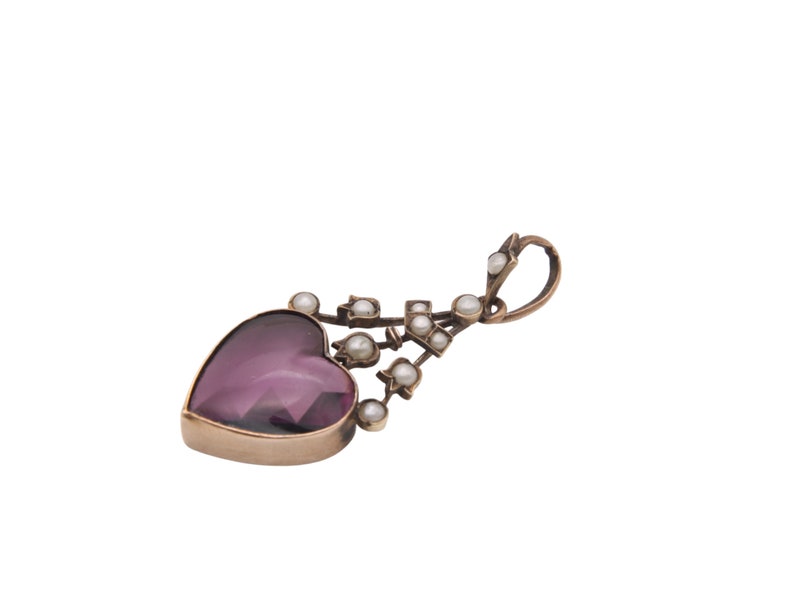 Puede incluir: Un colgante en forma de coraz&oacute;n con una piedra preciosa p&uacute;rpura facetada, enmarcada en oro. Peque&ntilde;as perlas redondas est&aacute;n dispuestas a lo largo de un tallo decorativo curvo. El colgante tiene un lazo para una cadena.