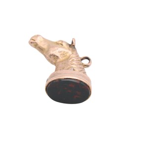 May include: A gold-toned horse head pendant with a dark red and black oval base. The horse head is detailed with a mane and a small loop for a chain. The pendant is likely vintage or antique.
