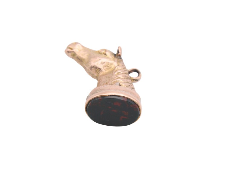 May include: A gold-toned horse head pendant with a dark red and black oval base. The horse head is detailed with a mane and a small loop for a chain. The pendant is likely vintage or antique.