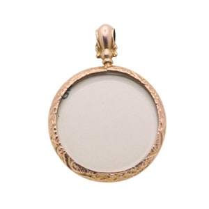 Op de afbeelding: Een goudkleurige, ronde hanger met een sierlijke, gegraveerde rand. De hanger heeft een blanco, gebroken witte midden en een decoratieve beugel aan de bovenkant. Het ontwerp suggereert een vintage of antieke stijl, geschikt voor sieraden.