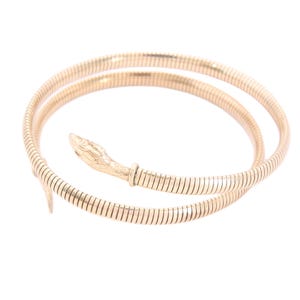 Pode incluir: Pulseira de cobra dourada. A pulseira enrola-se, com um design de cabeça de cobra numa extremidade. A cabeça da cobra é detalhada e a pulseira tem uma textura canelada. A joia está sobre um fundo branco.