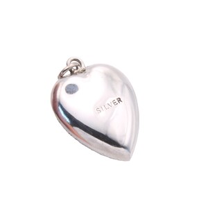 May include: A polished silver heart-shaped pendant with a small loop at the top for a chain. The word "SILVER" is stamped on the back of the pendant. The pendant is smooth and reflective.