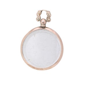 Op de afbeelding: Een ronde, antieke hanger met een helder midden en een roségoudkleurige rand. De hanger heeft een decoratieve, zilverkleurige lus aan de bovenkant om op te hangen. Het ontwerp is eenvoudig en elegant, geschikt voor sieraden.