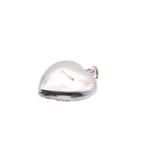May include: A silver heart-shaped charm with a small loop at the top for attachment. The word "SILVER" is stamped on the surface of the charm. The charm is smooth and reflective, with a rounded shape.