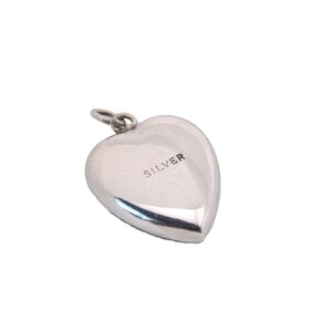 May include: A polished silver heart-shaped pendant with a small loop at the top for a chain. The word "SILVER" is stamped on the front. The pendant is a classic design, suitable for jewelry.