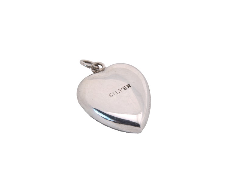 May include: A polished silver heart-shaped pendant with a small loop at the top for a chain. The word "SILVER" is stamped on the front. The pendant is a classic design, suitable for jewelry.