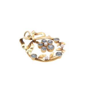 May include: A gold-toned pendant with a bow design and a cluster of light blue gemstones and small pearls. The pendant has a loop at the top for a chain. The gemstones are set in gold bezels, and the overall design is floral.