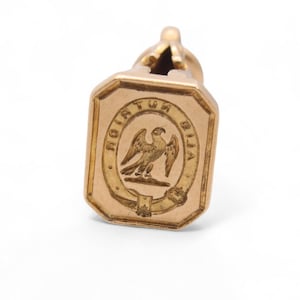 May include: A gold-colored antique fob seal with an octagonal face. The face features an engraved eagle within an oval, surrounded by the Latin inscription "ROTA TUR VITA". The seal has a loop at the top.