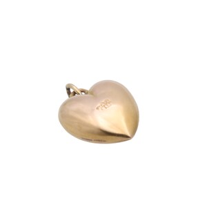 May include: A gold-colored heart-shaped pendant with a small loop at the top for a chain. The pendant has a smooth, polished surface and a rounded shape. The heart is slightly tilted, showcasing its three-dimensional form.