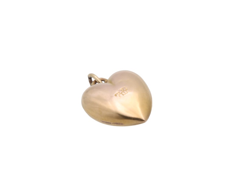 May include: A gold-colored heart-shaped pendant with a small loop at the top for a chain. The pendant has a smooth, polished surface and a rounded shape. The heart is slightly tilted, showcasing its three-dimensional form.