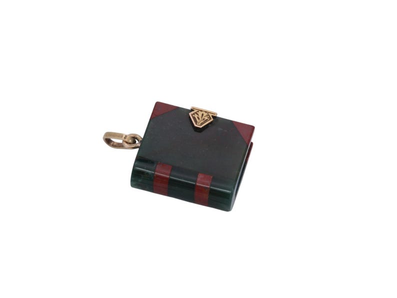 May include: A small, book-shaped pendant with a gold-colored clasp and chain. The pendant is primarily dark green with red and gold accents. The clasp features a decorative design.