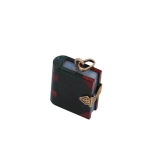 May include: A miniature book pendant with a gold-colored bail and clasp. The book has a dark green cover with red accents and a light blue interior. The clasp features an ornate design.