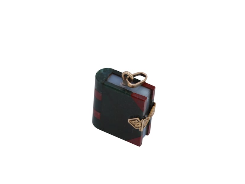May include: A miniature book pendant with a gold-colored bail and clasp. The book has a dark green cover with red accents and a light blue interior. The clasp features an ornate design.