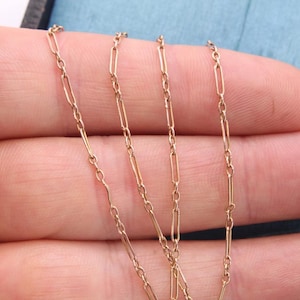 K&ouml;nnte beinhalten: Nahaufnahme einer zarten Goldhalskette mit einem Paperclip-Kettendesign. Die Halskette wird vor einem hellblauen Hintergrund pr&auml;sentiert. Die Kette besteht aus kleinen, rechteckigen Gliedern.