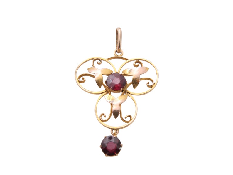 May include: A gold-toned pendant with a floral design and three circular elements. The pendant features three round, deep red gemstones and a smaller, dangling gemstone at the bottom. The design includes leaf-shaped accents.