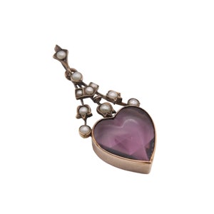 Puede incluir: Colgante antiguo con una piedra de amatista en forma de coraz&oacute;n. El colgante est&aacute; adornado con peque&ntilde;as perlas y una montura de metal dorado. El dise&ntilde;o incluye una cadena decorativa con perlas, creando una est&eacute;tica vintage elegante.