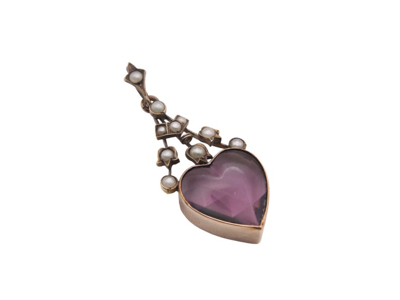 Puede incluir: Colgante antiguo con una piedra de amatista en forma de coraz&oacute;n. El colgante est&aacute; adornado con peque&ntilde;as perlas y una montura de metal dorado. El dise&ntilde;o incluye una cadena decorativa con perlas, creando una est&eacute;tica vintage elegante.