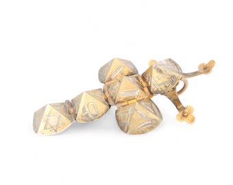 Könnte beinhalten: Ein antiker goldfarbener Metallanhänger mit geometrischen Formen und geätzten Designs. Der Anhänger zeigt eine Reihe von verbundenen pyramidenartigen Formen und ein kreuzförmiges Element. Die komplizierten Details und das gealterte Aussehen deuten auf ein Vintage-Stück hin.