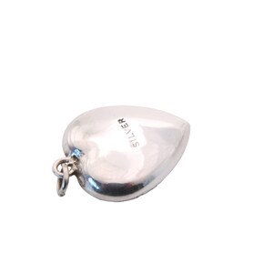 May include: A polished silver heart-shaped pendant with a small loop for a chain. The word "SILVER" is stamped on the surface. The pendant is a classic jewelry piece, suitable for various occasions.