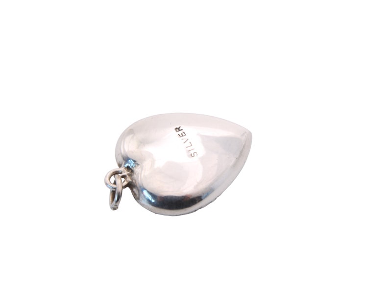 May include: A polished silver heart-shaped pendant with a small loop for a chain. The word "SILVER" is stamped on the surface. The pendant is a classic jewelry piece, suitable for various occasions.