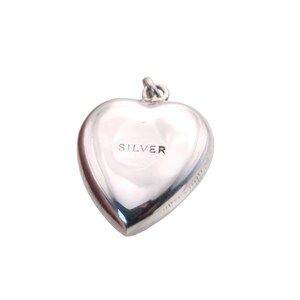 May include: A polished silver heart-shaped charm with the word "SILVER" engraved on the front. The charm has a loop at the top for attaching to a necklace or bracelet. The charm is a classic and timeless piece of jewelry.