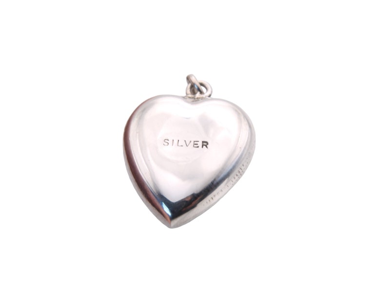 May include: A polished silver heart-shaped charm with the word "SILVER" engraved on the front. The charm has a loop at the top for attaching to a necklace or bracelet. The charm is a classic and timeless piece of jewelry.