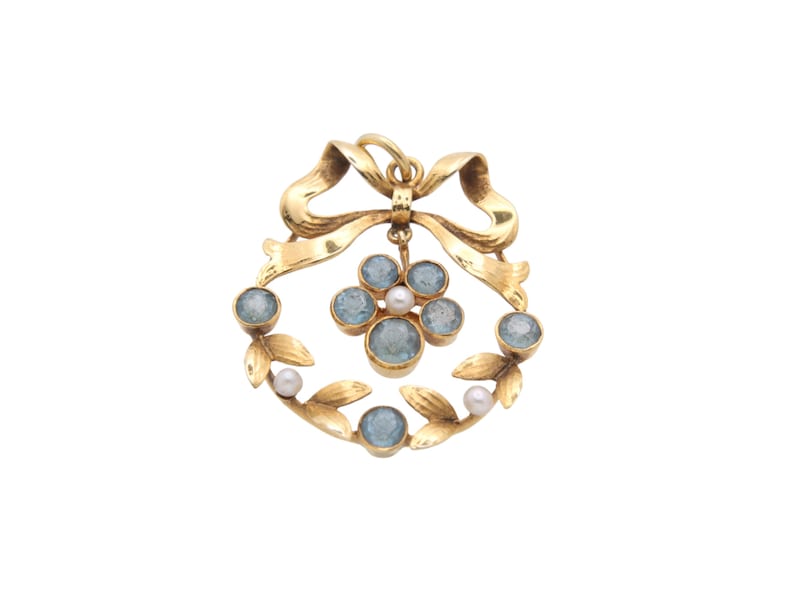 May include: A gold-toned pendant featuring a bow, a wreath of leaves, and a cluster of gemstones. The pendant has a central arrangement of blue gemstones and pearls, surrounded by additional blue gemstones. The bow is at the top.