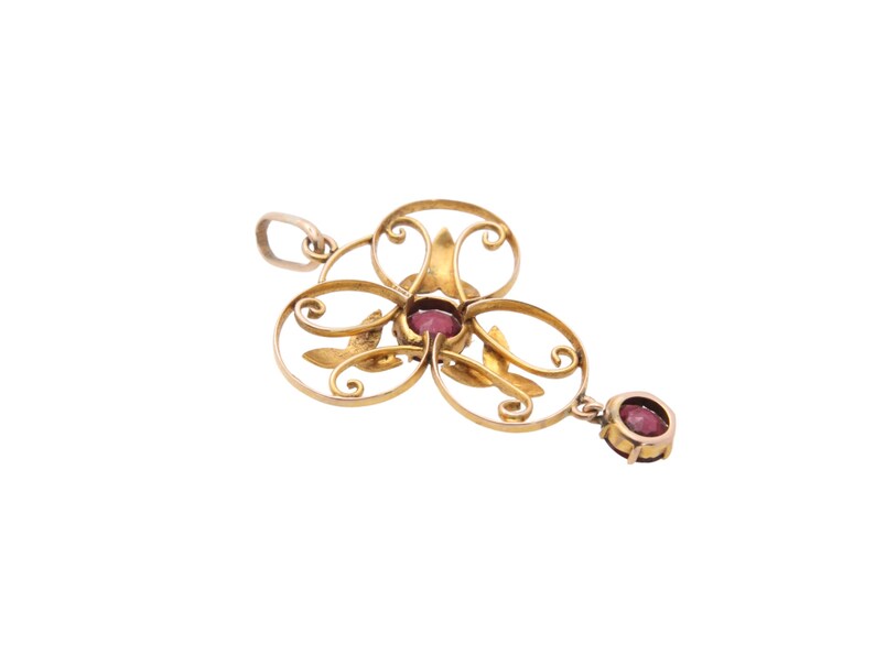 May include: A gold-toned pendant with a floral design, featuring a cluster of oval shapes and leaf accents. The pendant is adorned with several round, deep red gemstones. A single gemstone hangs from the bottom.
