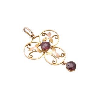 May include: A gold-toned pendant with a floral design, featuring three circular elements with red gemstone centers and a dangling gemstone. The pendant has a delicate, openwork design with a small loop for a chain.