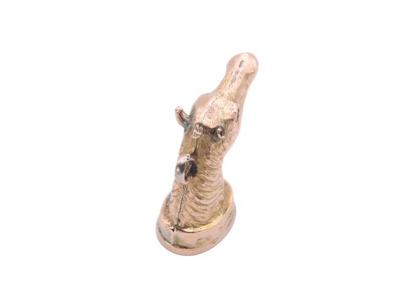 May include: A bronze-colored hippo figurine. The hippo's head is tilted upwards, with detailed features including ears, eyes, and textured skin. The figurine is mounted on a small, oval base. The overall design is detailed and artistic.