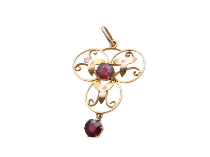 May include: A gold-toned pendant with a floral design and three circular elements. Each circle holds a round, deep red gemstone. A fourth gemstone dangles below. The pendant has a loop at the top for a chain.