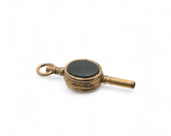 May include: A gold-toned antique watch key with an oval, dark green stone inset with red flecks. The key has a loop at one end and a winding mechanism at the other. The key is set against a white background.