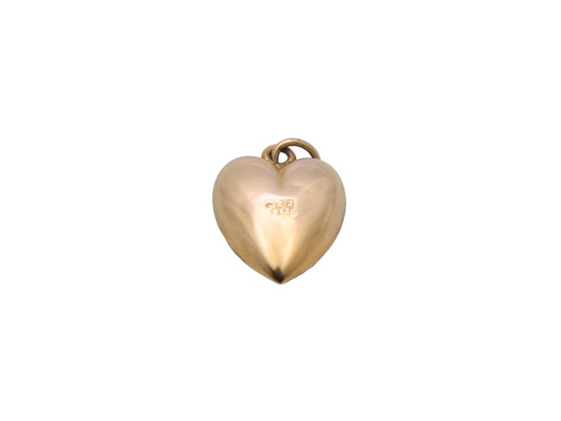 May include: A gold-colored heart-shaped pendant with a small loop at the top for a chain. The pendant has a smooth, polished surface and a subtle inscription on the front. The heart shape is rounded and symmetrical.