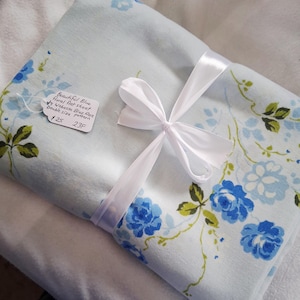 May include: A pale blue floral flat sheet, patterned with blue roses and green leaves, tied with a white ribbon. The tag reads "Beautiful Blue floral flat sheet by Wabesse Blue Rose Double size pattern."