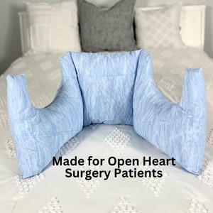 May include: A light blue wedge-shaped pillow with two armrests. The pillow is made for open heart surgery patients.
