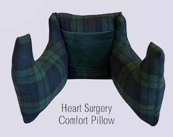 May include: A dark green and navy blue plaid comfort pillow with two side arms and a central pocket. The text Heart Surgery Comfort Pillow is printed in black below the pillow. The design features a structured shape with a soft fabric finish.