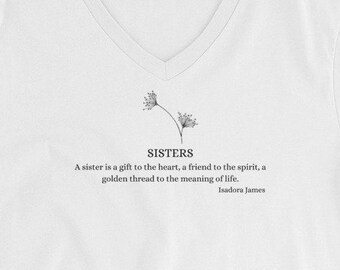 May include: White V-neck t-shirt featuring the word "SISTERS" and a floral design. The quote by Isadora James reads, "A sister is a gift to the heart, a friend to the spirit, a golden thread to the meaning of life."