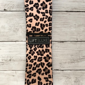 May include: A pink and black leopard print resistance band with the text "LIFT LUXE" printed on the band.