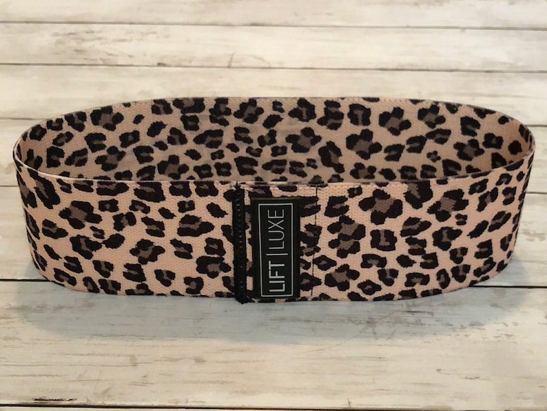 May include: A pink and black leopard print resistance band with the text "LIFT LUXE" printed on the band.