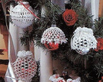May include: Five crocheted white Christmas ornaments with red glass balls inside. The ornaments are hanging on a Christmas tree.